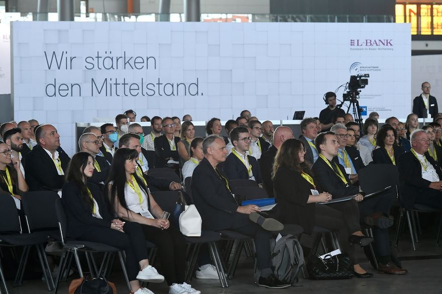 Nahaufnahme eines Publikums in mehreren Sitzreihen, im Hintergrund ist ein Banner mit der Aufschrift Wir stärken den Mittelstand mit dem L-Bank-Logo zu erkennen.