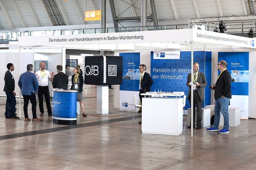 Mehrere Menschen stehen an einem Stand und unterhalten sich, der Schriftzug Die Industrie- und Handelskammern in Baden-Württemberg ist zu sehen.