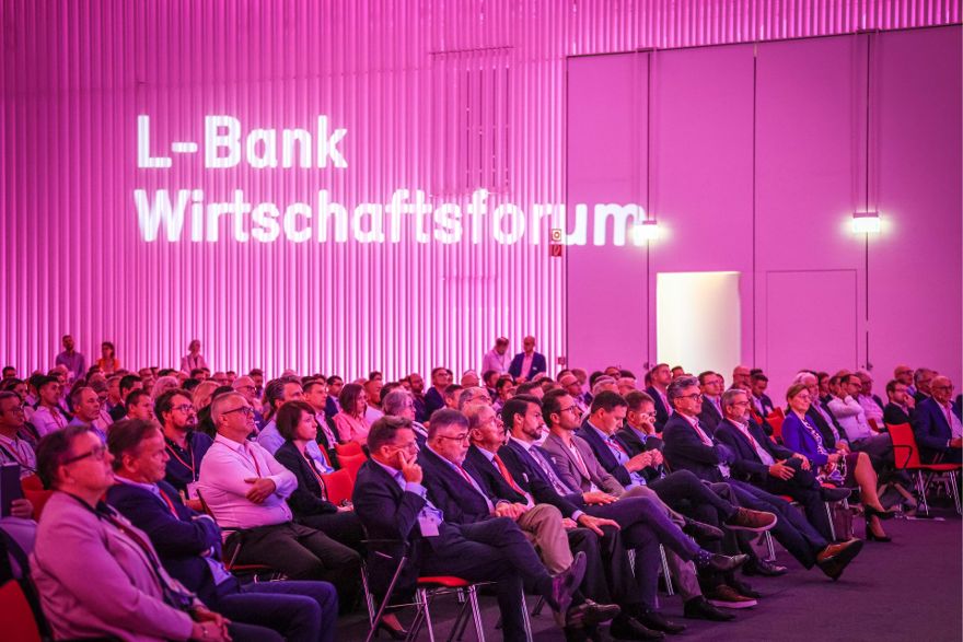 Mehrere Reihen sitzender Menschen, die konzentriert in eine Richtung schauen. Im Hintergrund ist der Schriftzug L-Bank Wirtschaftsforum zu sehen.